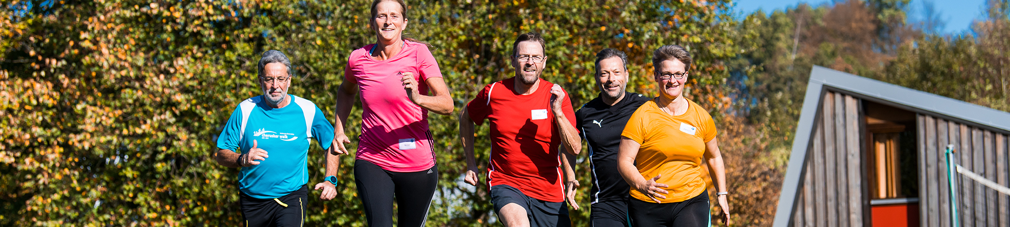 Drei Männer und und zwei Frauen in Sportkleidung joggen auf die Kamera zu.
