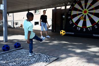 Ein kleiner Junge im türkisen T-Shirt und blauer Jeans schießt einen gelben Ball auf eine überdimensional große Dartscheibe. Eine Mitarbeiterin des Kreissportbundes schaut ihm dabei zu.
