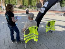 Ein älterer Mann mit dem Rücken zur Kamera, sitzend auf einem Stuhl, während eine Mitarbeiterin des Kreissportbundes mit einem Flyer neben ihm steht und erklärt.